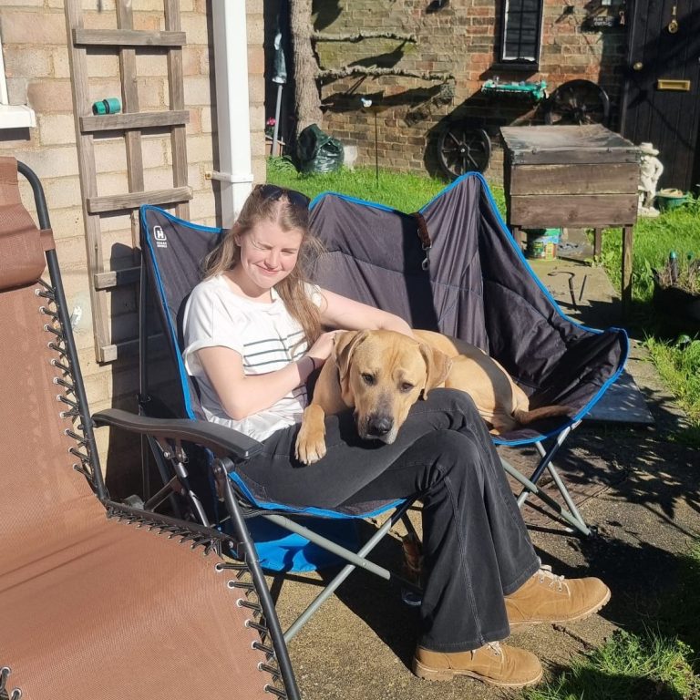 Young girl sitting on a chair with a Labrador dog on her lap in a garden setting.